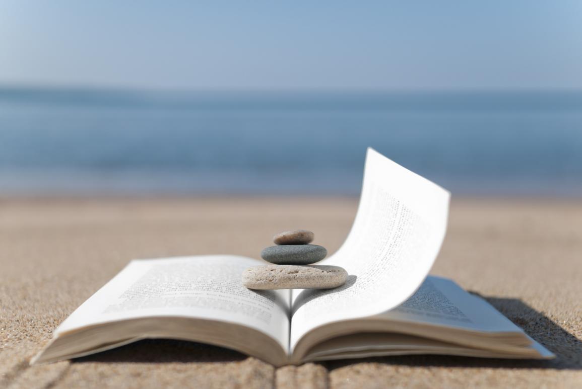 livre ouvert et galets posés dessus sur une plage - hotel la baule escoublac